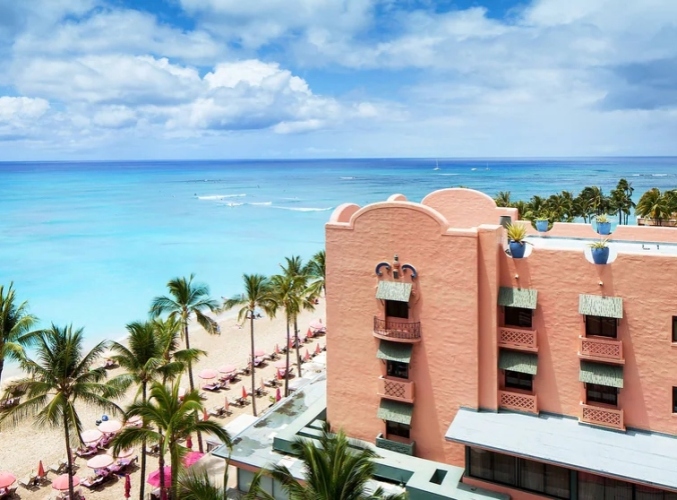 Exterior view of The Royal Hawaiian on Waikiki Beach with the blue ocean beyond.
