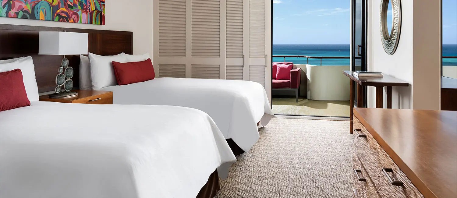 Twin bedroom with double beds and a balcony overlooking Waikiki Beach.