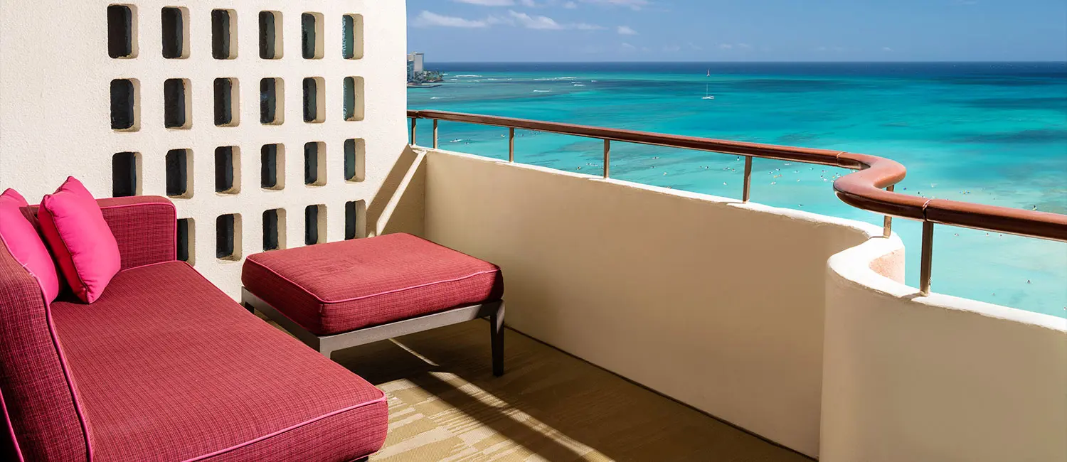 Balcony with pink sofa offering panoramic views of Waikiki Beach.
