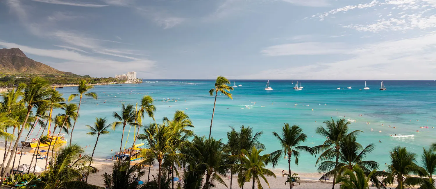 Emerald-blue Waikiki Beach with palm trees and sailing boats.