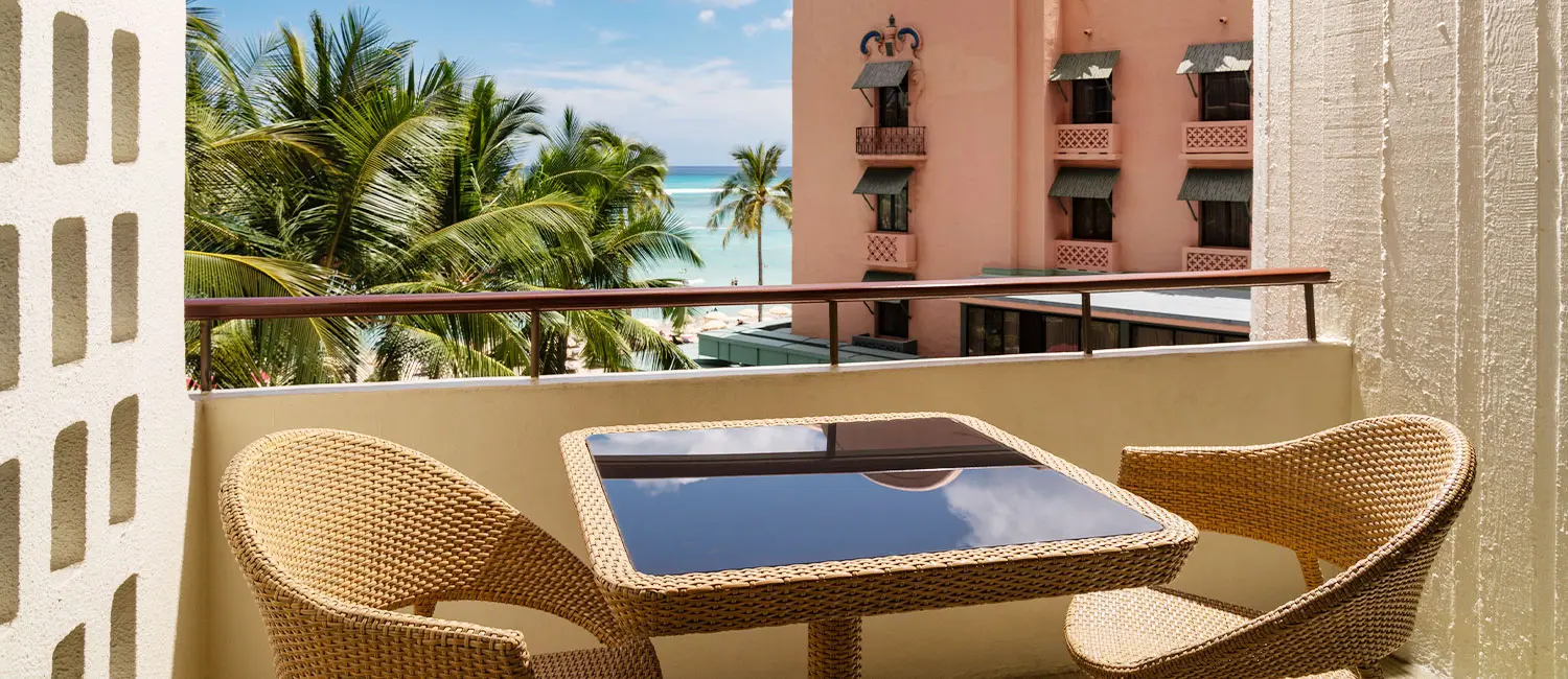 Balcony with view of the pink façade, palm trees, and Waikiki’s ocean.