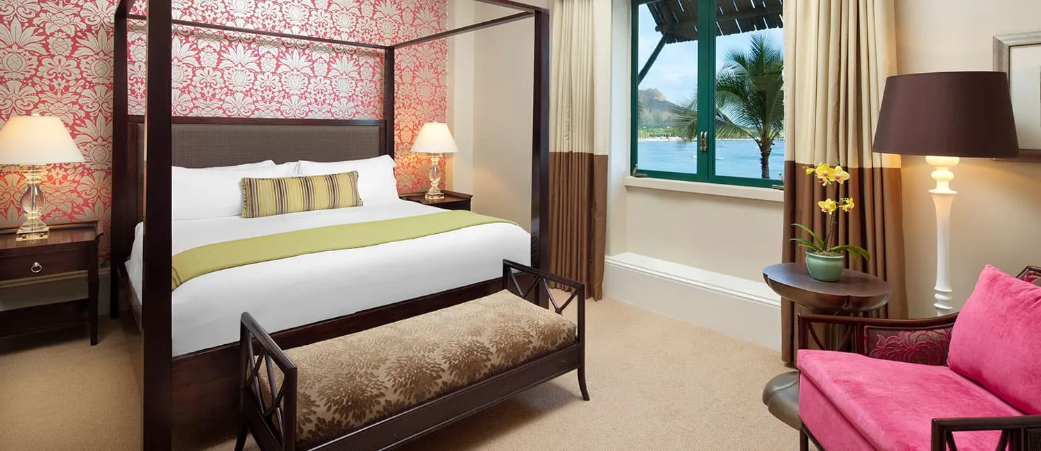 Bedroom with red patterned wallpaper and an ocean view through large windows.